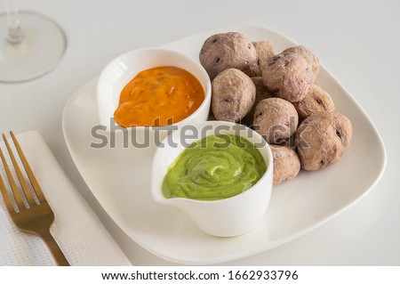 Canary Islands pdish Papas Arrugadas ( wrinkly potatoes) with Mojo picon (Red hot sauce) and  Mojo verde ( Green sauce)  on restaurant table   Royalty-Free Stock Photo #1662933796
