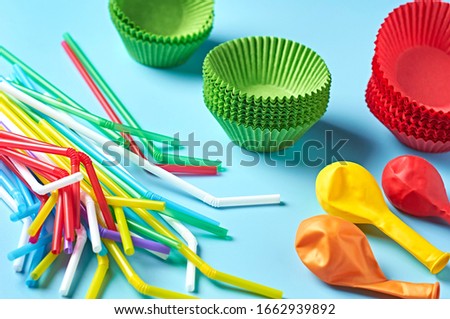 Different color paper molds for baking muffins, balloon and straw scattered on blue desk on kitchen. Close-up