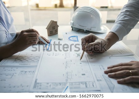 Two architect working at construction site and compass drawing pointing on blueprint with partnership.