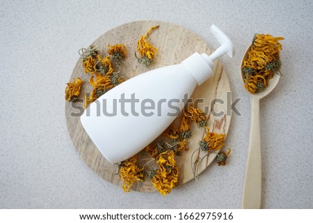               
white bottle with a soap dispenser with dried flowers of medicinal calendula on a wooden plate with a wooden spoon on a light background                 