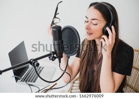 Attractive young woman blogger with long black hair recording online podcast using her laptop, headphones and professional microphone.