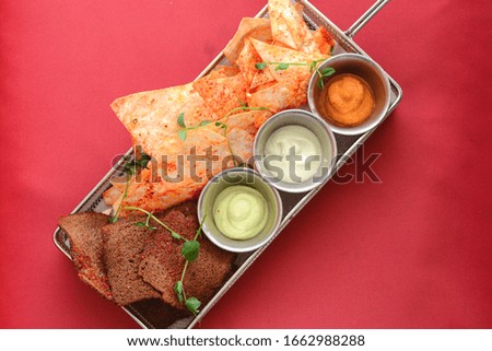 Nachos tortilla chips and different kinds of sauce in a tray on dark wooden board. Fast food, junk food, beer snack concept. Nachos and tomato dip.