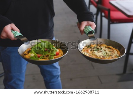 Man holds two pans. English breakfast - fried egg, beans, tomatoes, mushrooms, seeds served in a pan. Top view, copy space. Healthy breakfast, diet.