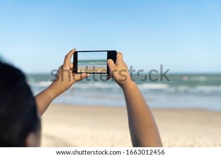 Woman traveler using smartphone and taking photo of sea beach.