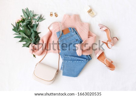 Blue jeans, pink knitted sweater, heeled sandals, small bag and bouquet of flowers lie on white background. Overhead view of woman's casual outfit. Trendy stylish women clothes. Flat lay, top view. Royalty-Free Stock Photo #1663020535