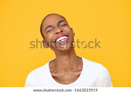 Happy optimistic African American woman laughing with eye closed isolated on colorful yellow background