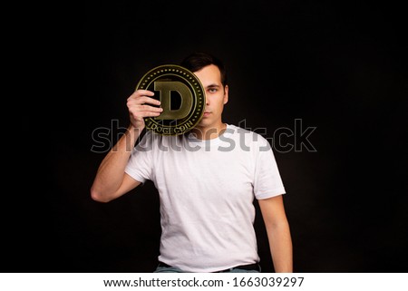 A young guy holds a symbol of the dogecoin coin, a modern currency for exchange and purchases. Photo on a black background.