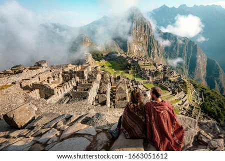 Couple dressed in ponchos watching the ruins of Machu Picchu Royalty-Free Stock Photo #1663051612