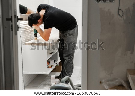 man drills a washbasin hole in the bathroom,home repair work in the bathroom,puncher at work,drill Royalty-Free Stock Photo #1663070665