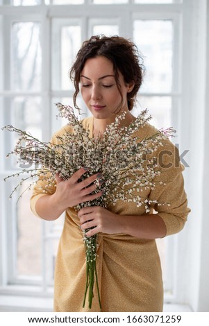 girl with a bouquet stands on a background of a window