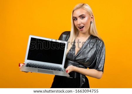 surprised girl holds laptop with template for web page on yellow background