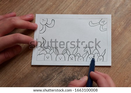 Children's easter drawing card on the wooden background. Few painted rabbits on a white card