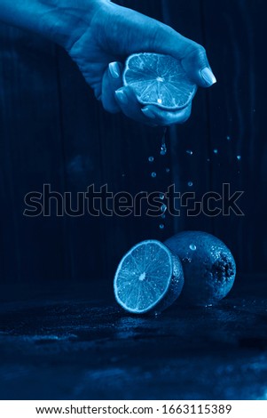 lime fruit on a classic blue background in a low key with a female hand that squeezes the juice from a lemon slice
