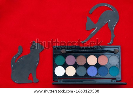 Makeup flat lay on the red background. Multicolored eye shadow and stencils in the form of a cat for drawing eye lines.