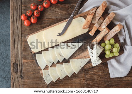 Top view, cheese platter with baguette and grapes on wooden table with ingredients around