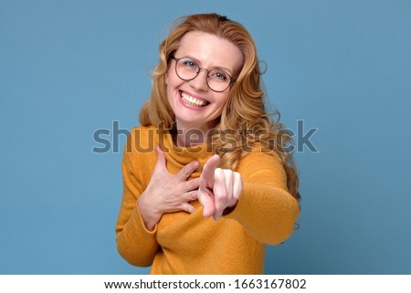 Happy mature woman in glasses pointing at you. I choose you. Studio shot on blue wall.
