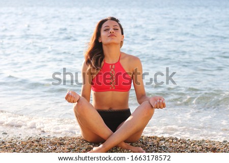 Meditation - Yoga woman meditating at serene beach sunset. Girl relaxing in lotus pose in calm zen moment in the ocean water during yoga holidays resort retreat. Multiracial girl.