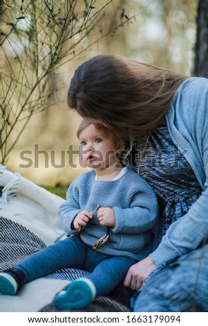 mom with her little daughter in gray clothes sitting in the forest. little happy, smiling baby and mom. a gentle family photo. mom and daughter without makeup and very long hair. natural  beauty
