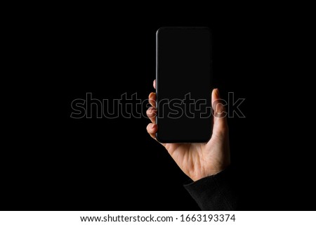 Person holding in hand smartphone, isolated on black background Royalty-Free Stock Photo #1663193374