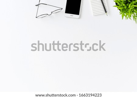 Overhead shot of mobile phone, notebook, pen and eyeglasses on white table with copyspace. Office desktop. Flat lay