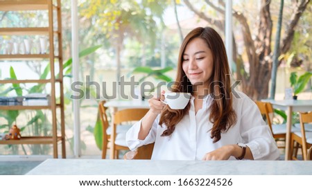 Closeup image of a beautiful asian woman holding and drinking hot coffee with feeling good in cafe