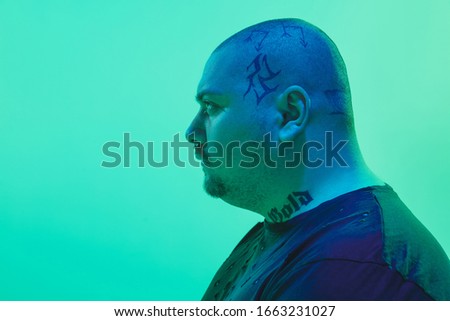 Attented. Portrait of a guy with colorful neon light on green studio background. Male model with calm mood. Facial expression, cyberpunk, millenials lifestyle and look like. Future, technologies.