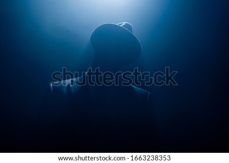 Silhouette of dangerous gangster in suit and felt hat on dark background Royalty-Free Stock Photo #1663238353