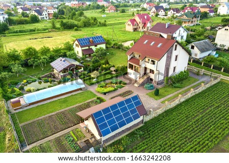 Aerial view of a private house in summer with blue solar photo voltaic panels on roof top and green yard.