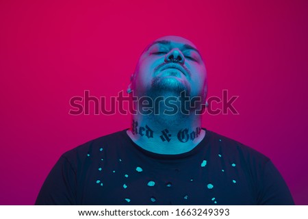 Portrait of a guy with colorful neon light on red studio background. Male model with calm and serious mood. Facial expression, cyberpunk, millenials lifestyle and look like. Future, technologies.