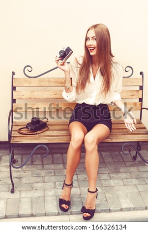 Outdoor fashion portrait of pretty smiling woman in city sitting on bench in summer