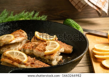 Portioned pieces of fried fish in a black cast-iron pan with fresh cucumbers and herbs. Traditional dinner of a village fisherman