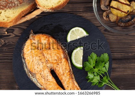 Grilled salmon steak on a black slate dish with parsley and lime