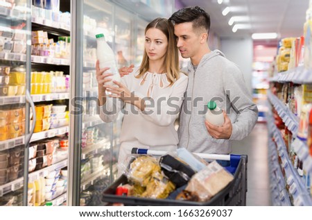 Young  cheerful positive smiling female and male customers choosing milk and dairy products in grocery, family shopping