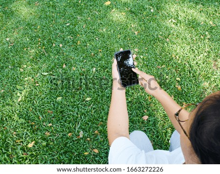 Woman holding and touch smartphone with blank screen while relaxing in the park.