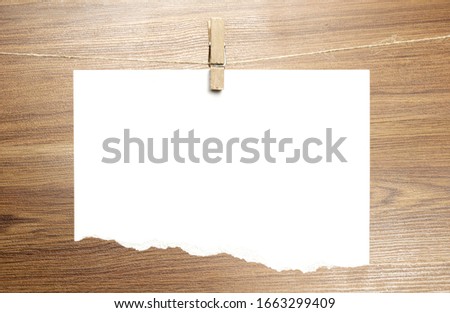 Empty torned paper sheet frame that hang on a rope with clothespins and on wooden background. Blank cards on rope. Mockup template for memories backdrop, photos, social media etc.