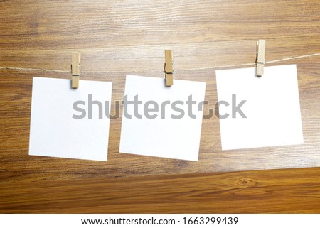 Empty paper sheets for notes, frames that hang on a rope with clothespins on wooden background. Blank cards on rope. Mockup template for memories backdrop, photos, social media etc.