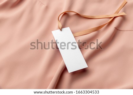 White clothing tag, label blank mockup template with the ribbon, to place your design. On a premium cotton pink fabric textile background