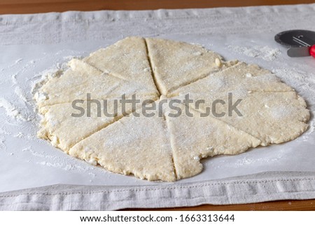 Rolled raw curd dough with bits of cottage cheese cut into eight triangles sprinkled with sugar on baking paper on a linen tablecloth on a wooden table. The process of making curd bagels or croissants