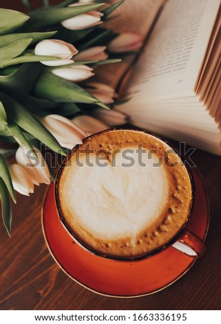 Coffee cup in the frame of white tulips on a wooden base.  Flat lay, top view.  The concept of the holiday, birthday, Easter, March 8.  Morning with a book in a coffee shop