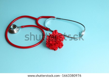 A red stethoscope on a blue background and a red carnation symbolize the national day of the doctor Royalty-Free Stock Photo #1663380976