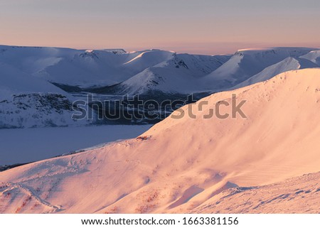 Colorful snow-capped mountains on the shore of a frozen lake at sunset in in the Arctic. Russia, Murmansk region