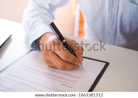 A business man sitting at a desk signing contract with an emphasis on the signature.
