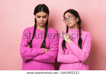 Image of two offended teenage girls with braids in casual clothes standing with arms crossed isolated over pink background