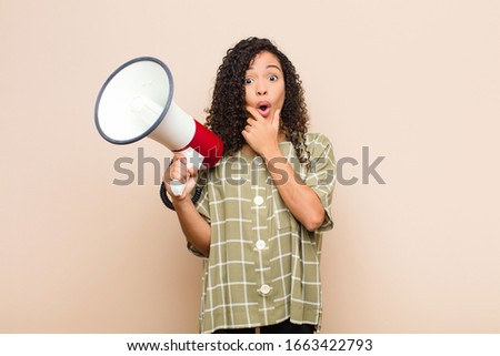 young black woman with mouth and eyes wide open and hand on chin, feeling unpleasantly shocked, saying what or wow holding a megaphone