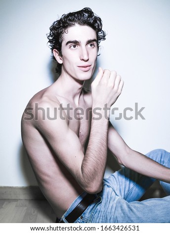 expressive mediterranean Italian young dark haired handsome male model boy posing for casual fashion shooting wearing blue jeans and sitting on wooden floor