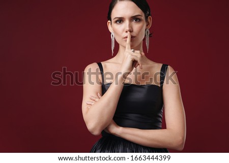 Beautiful young brunette woman wearing cocktail dress and accessories standing isolated over burgundy background, showing silence gesture