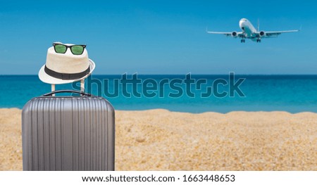 Summer travel and plan with black suitcase luggage with hipster hat and sunglasses on tropical sea and sandy beach, airplane and blue sky background. Summer holiday traveling design concept.
