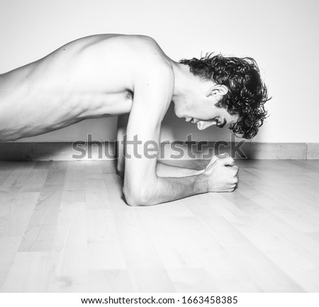 black and white photography.mediterranean Italian dark haired handsome male model boy with angel face and fit sportive shaped body exercising in Plank position on wooden floor and white background