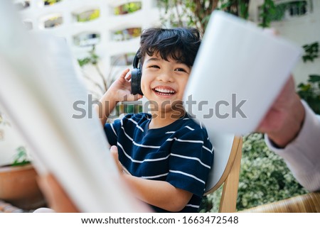 Little boy wearing the headphone and watching the cartoon on internet with smartphone while sitting in the backyard with grandpa.