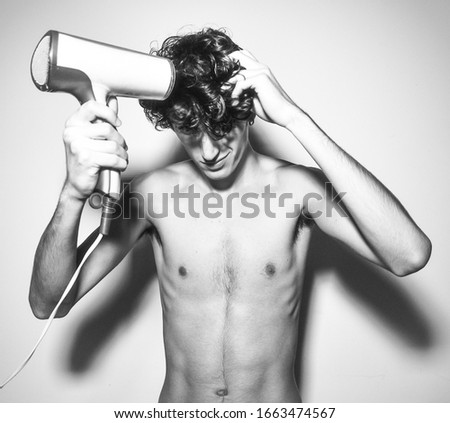 black and white photography.expressive mediterranean Italian dark haired handsome male model boy with angel face and fit sportive shaped body playing with hair blower 